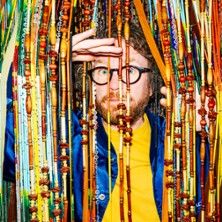 Ein Mann mit Brille schaut durch bunte Perlenvorhänge.