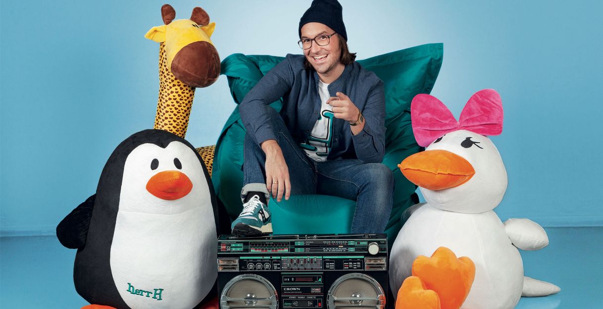 Ein Mann sitzt auf einem Sitzsack, umgeben von großen Plüschtieren und einem Ghettoblaster.