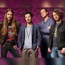 Vier Männer stehen vor einem lila Hintergrund, lässig gekleidet.