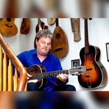 Ein Mann spielt Gitarre auf einer Treppe, umgeben von verschiedenen Gitarren an der Wand.