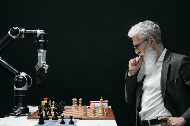 Ein Mann mit weißem Bart spielt Schach gegen einen Computer.