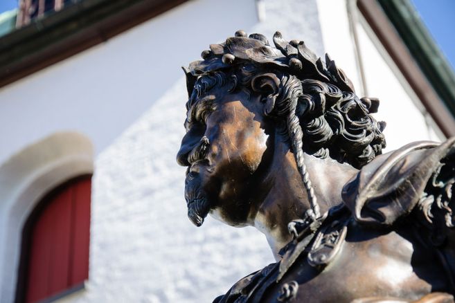 Nahaufnahme einer Bronzestatue mit Lorbeerkranz vor einem Gebäude.