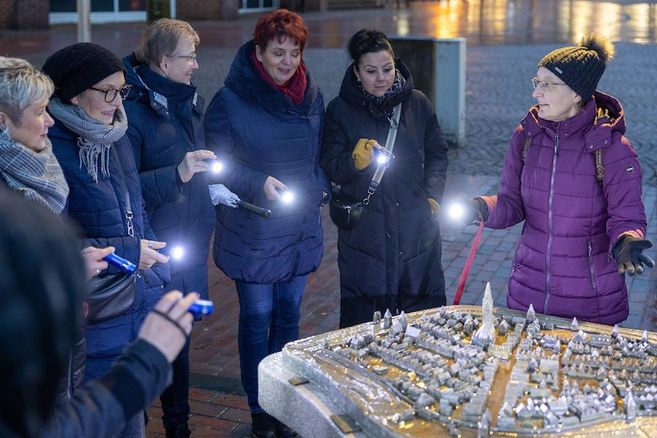 Gruppe von Frauen bei einer historischen Stadtführung mit Taschenlampen an einem beleuchteten Stadtmodell im Freien.