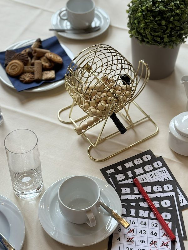Ein Tisch mit einer Bingo-Trommel, Bingo-Karten, einer Tasse Kaffee und Keksen.
