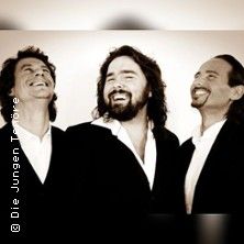 Drei Männer in Anzügen lachen und schauen nach oben.