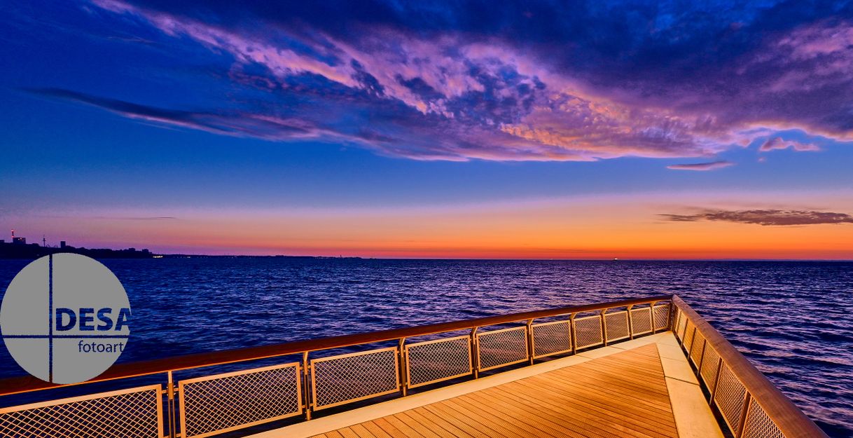 Eine Seebrücke erstreckt sich über das Meer bei Sonnenaufgang, mit einem farbenfrohen Himmel in Blau- und Orangetönen.