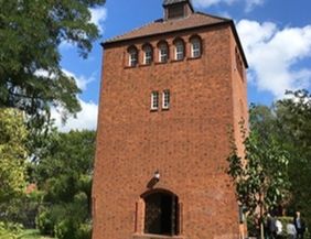 Backsteinturm mit Bäumen und blauem Himmel im Hintergrund.