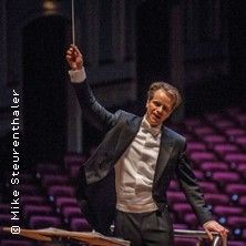 Ein Dirigent in einem Konzertsaal hebt den Taktstock, um ein Orchester zu dirigieren.