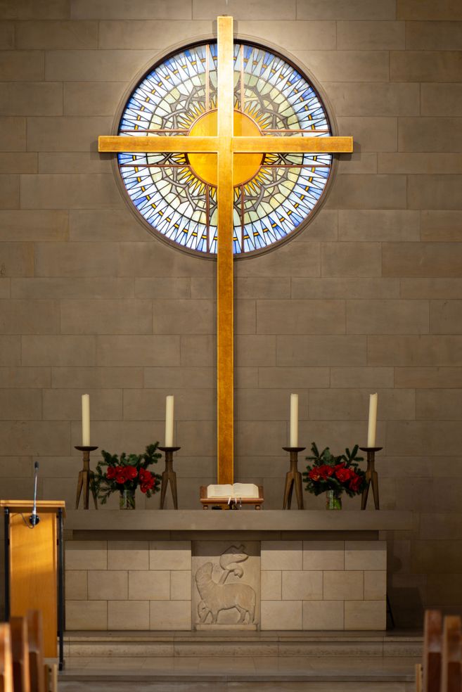 Kirchenaltar mit großem Holzkreuz und buntem Glasfenster im Hintergrund.