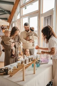 Eine Familie mit zwei kleinen Kindern steht an einem Tisch mit Produkten, während eine Frau ihnen etwas zeigt.