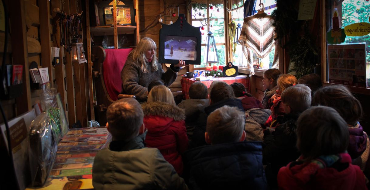 Eine Frau erzählt einer Gruppe von Kindern eine Geschichte in einer gemütlichen Holzhütte.