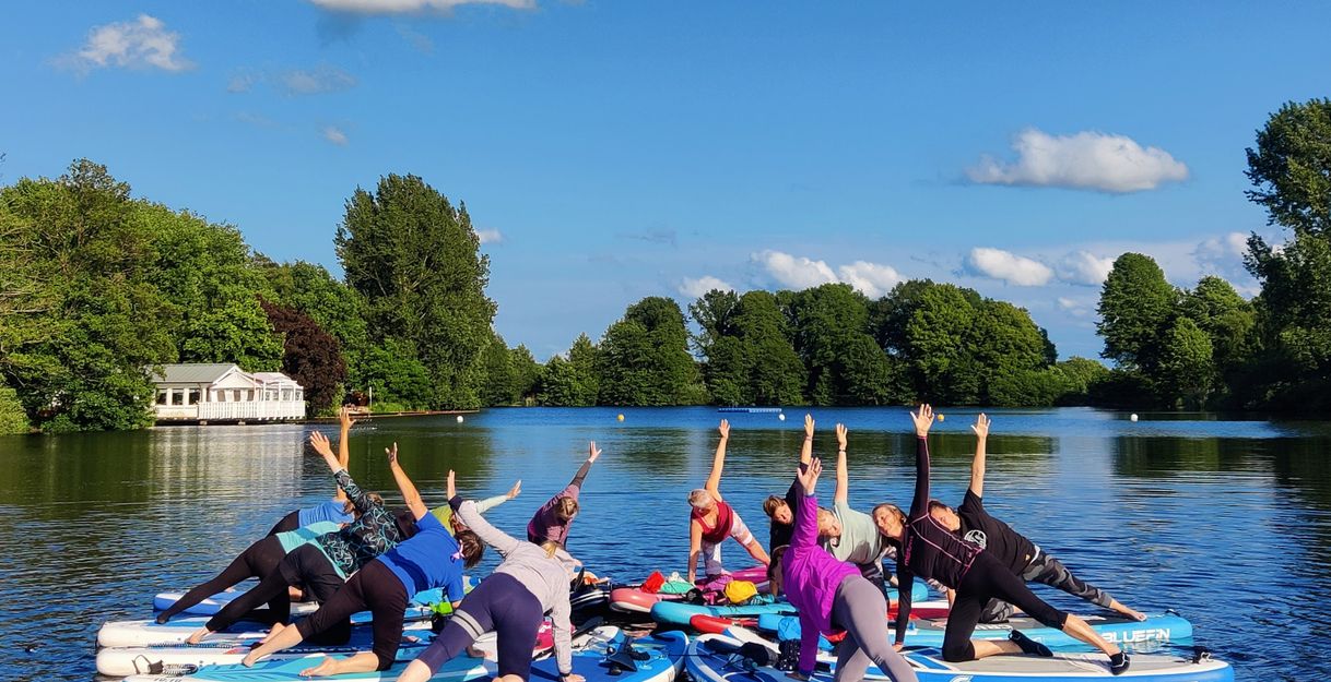 Gruppe von Menschen macht Yoga auf Stand-Up-Paddle-Boards auf einem See.