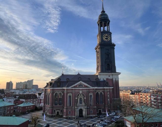Ansicht der St. Michaelis Kirche in Hamburg bei Sonnenuntergang mit der Elbphilharmonie im Hintergrund.
