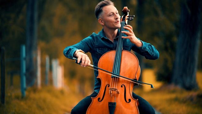 Ein Mann spielt Cello in einer herbstlichen Landschaft.