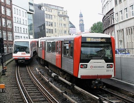 Zwei U-Bahn-Züge der Hamburger Hochbahn auf parallelen Gleisen in der Stadt.