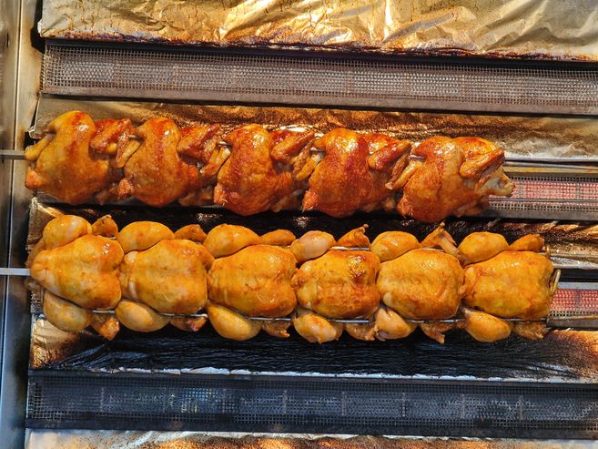 Zwei Reihen von Brathähnchen auf einem Grillspieß in einem Ofen.