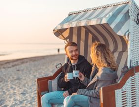 Ein Paar sitzt in einem Strandkorb am Strand und genießt Kaffee bei Sonnenaufgang.