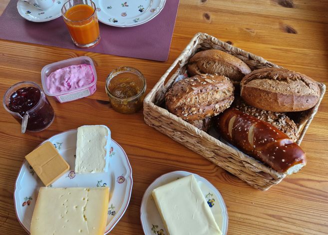Frühstückstisch mit Brötchen, Käse, Marmelade und Saft.