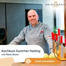 Ein Koch in grauer Uniform steht in einer modernen Küche neben einem Messerblock. Text: Kochkurs Summer Feeling mit Marko Bosse. Jetzt anmelden.