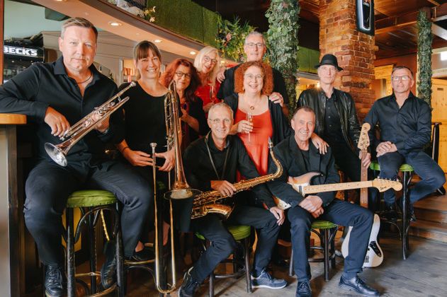 Eine Gruppe von Musikern posiert mit Instrumenten in einem gemütlichen Raum.