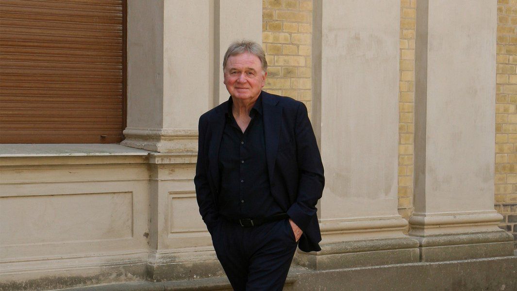 Ein Mann in dunklem Anzug steht vor einem Gebäude mit beiger Fassade.