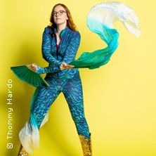 Eine Person in einem bunten Kostüm mit Fächern vor einem gelben Hintergrund.