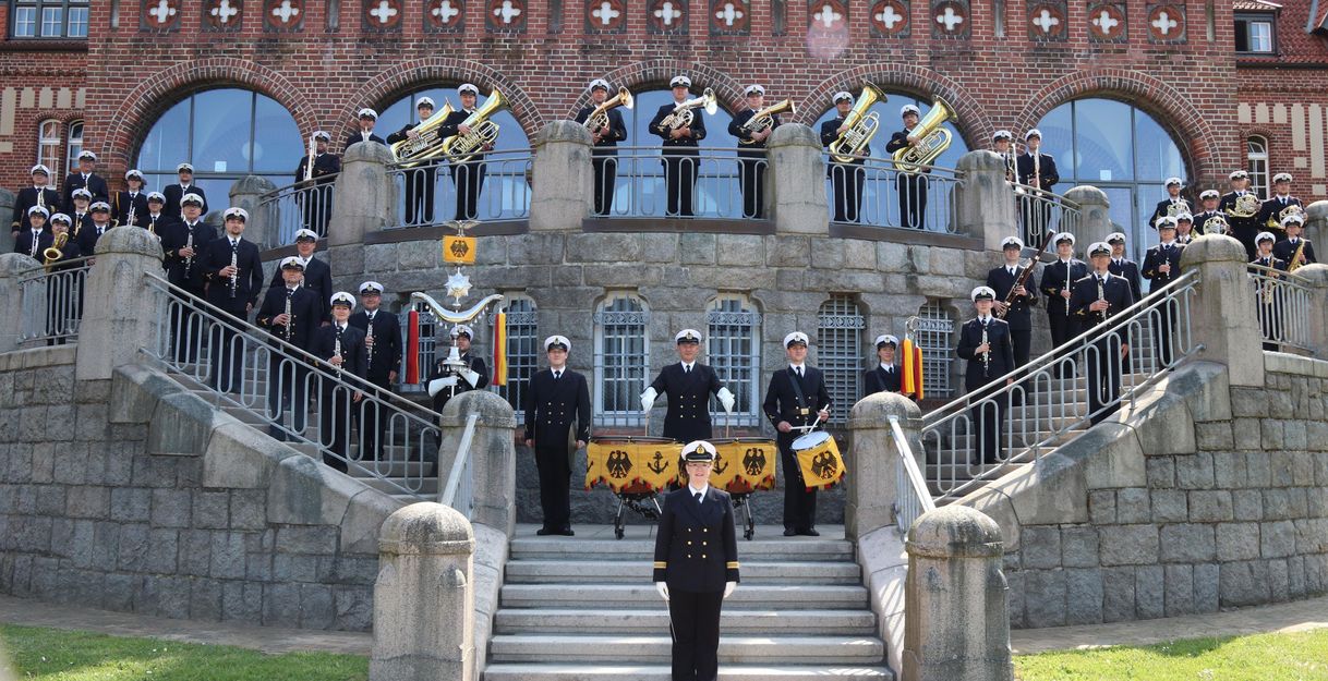 Das Marinemusikkorps Kiel posiert in Uniformen auf einer Treppe vor einem historischen Gebäude.