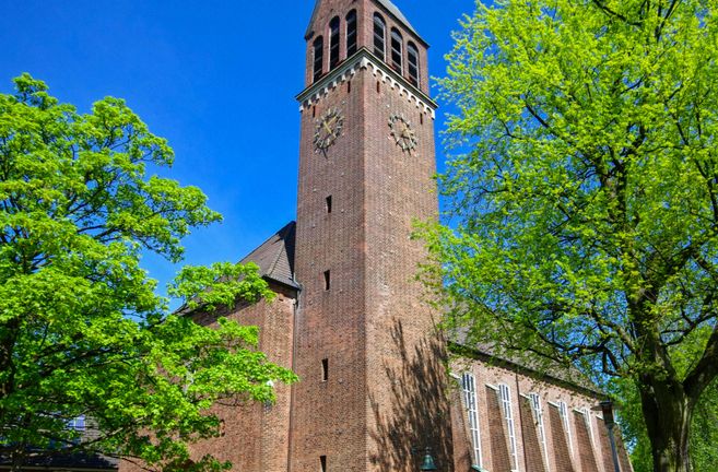 Backsteinkirche mit Turm und grünen Bäumen im Vordergrund.
