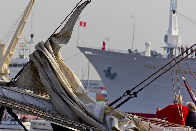 Segelboot mit gefalteten Segeln im Vordergrund, Frachtschiff im Hintergrund im Hamburger Hafen.