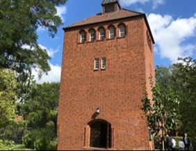 Backsteinturm mit Bäumen und blauem Himmel im Hintergrund.