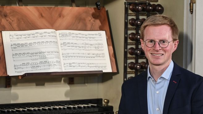 Ein Mann steht neben einer Orgel mit geöffnetem Notenbuch.