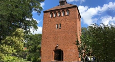 Backsteinturm mit Bäumen und blauem Himmel im Hintergrund.