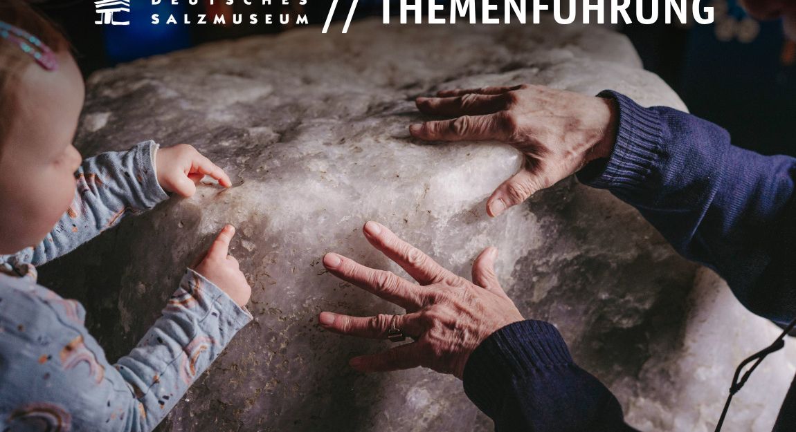 Ein Kleinkind und ein Senior berühren mit ihren Händen den großen Salzblock im Deutschen Salzmuseum.