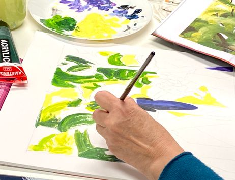 Eine Person malt die ersten Pinselstriche eines helles Bildes mit Acrylfarben in grün und violett