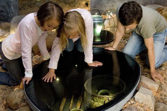 Drei Kinder betrachten Grabbeigaben in einem Museum.