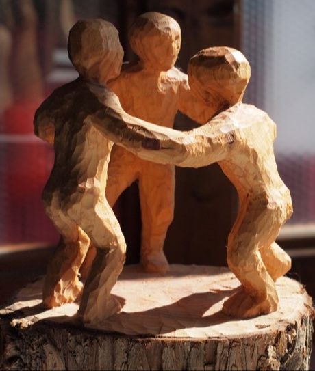 Holzskulptur von drei Menschen, die sich an den Händen halten und im Kreis stehen.