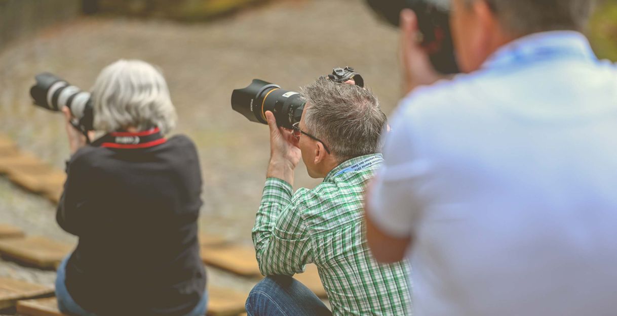 Drei Personen mit Kameras bei einem Fotoworkshop im Freien.