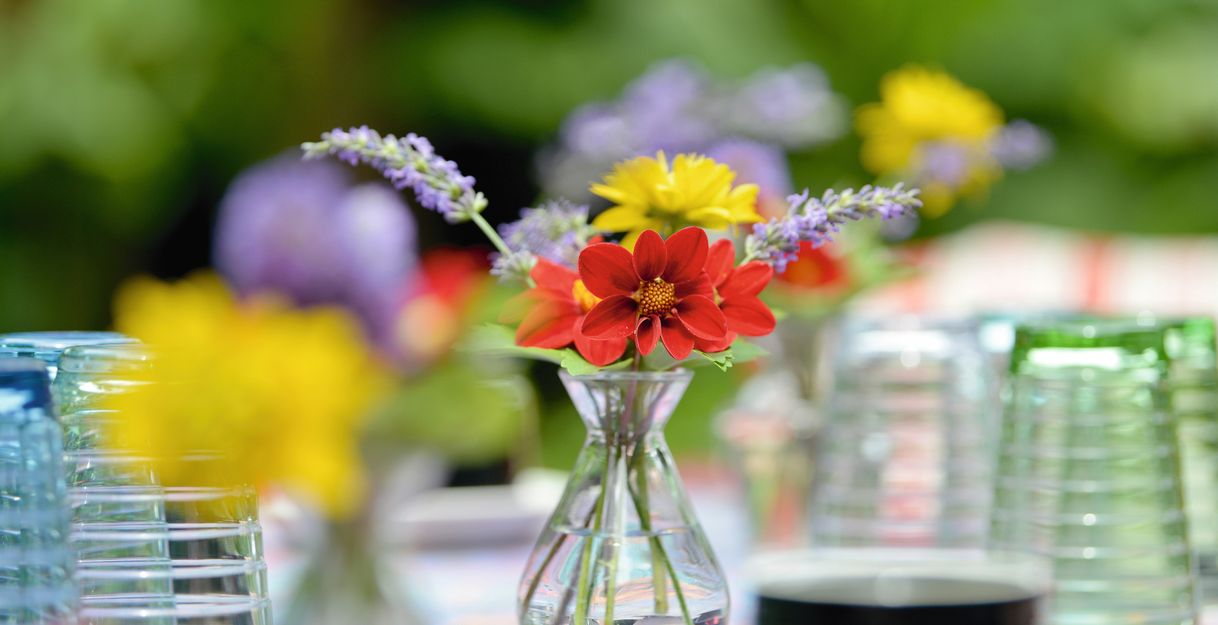 Ein Blumenstrauß in einer kleinen Vase auf einem Tisch mit Gläsern im Hintergrund.