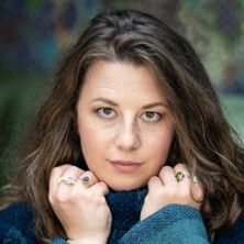 Porträt einer Frau mit langen braunen Haaren, die einen blauen Pullover hält.