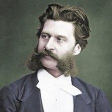 Porträt eines Mannes mit Bart und Anzug, vor neutralem Hintergrund.