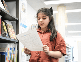 Ein Mädchen liest ein Blatt Papier in einer Bibliothek.