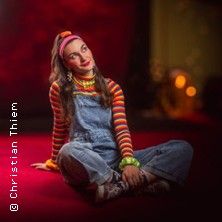 Eine Frau in bunter Kleidung sitzt auf einem roten Teppich und schaut nach oben.