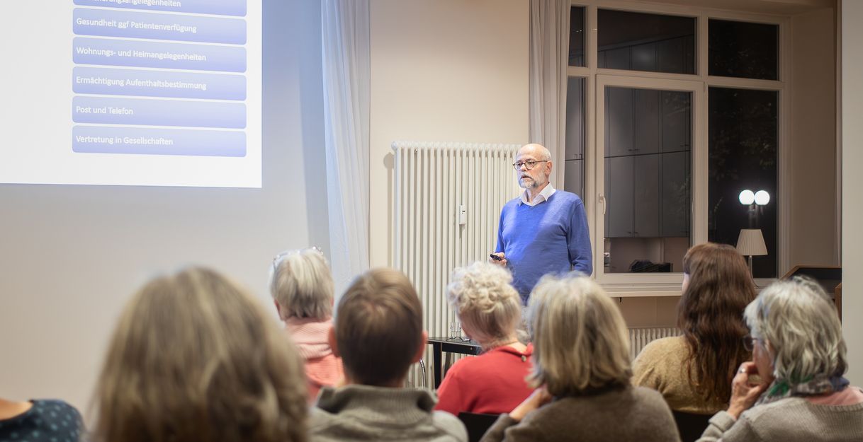 Rechtsanwalt Klaus Jakobsmeyer steht im Hamburg Leuchtfeuer Lotsenhaus vor einer Leinwand. Er spricht zu den Besuchenden der Veranstaltung "Vorsorge und Testament".