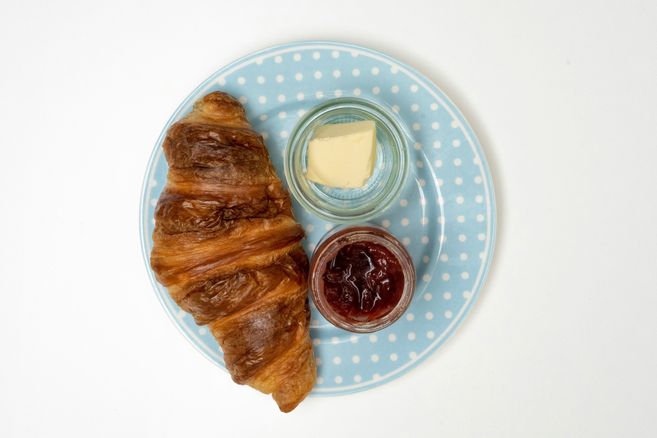 Ein Croissant mit Butter und Marmelade auf einem blauen Teller mit weißen Punkten.