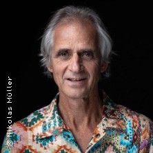 Porträt eines Mannes mit grauen Haaren und buntem Hemd vor schwarzem Hintergrund.