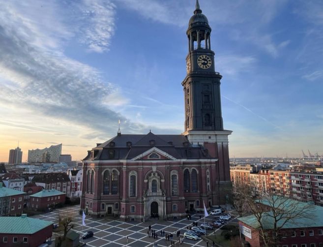 Die Kirche St. Michaelis in Hamburg bei Sonnenuntergang, mit der Elbphilharmonie im Hintergrund.