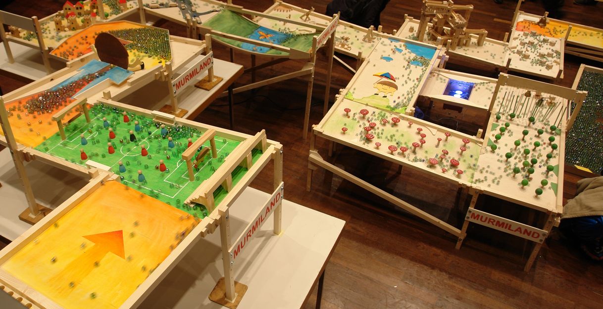 große Murmelbahn mit vielen unterschiedlich gestalteten Feldern, über die Mengen an Glasmurmeln kullern