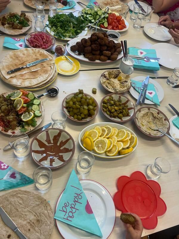 Tisch mit Speisen beim Interkulturellen Frauenfrühstück: Fladenbrot, Dips, Oliven, Gurken, Tomaten, Zitronenscheiben und Wassergläser, dazu Hände von Teilnehmenden.