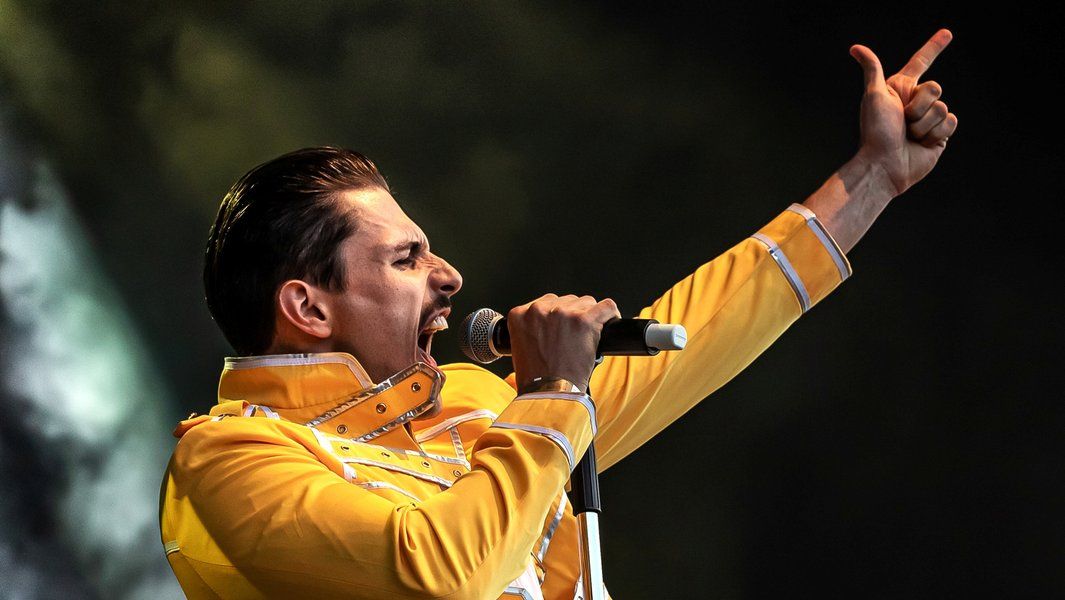 Sänger in gelber Jacke singt leidenschaftlich in ein Mikrofon auf der Bühne.