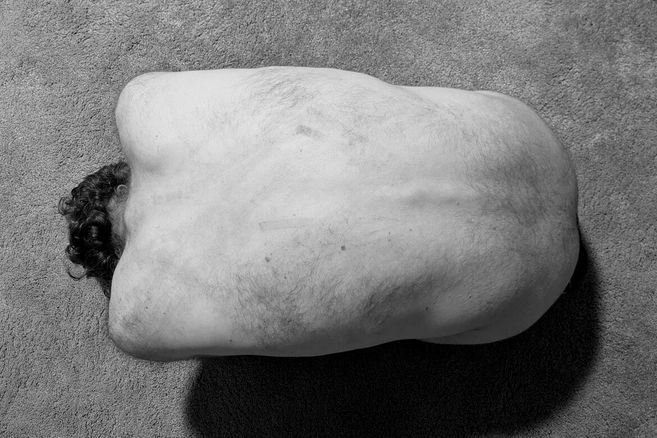 Schwarz-Weiß-Foto eines nackten Rückens einer Person, die auf einem Teppichboden liegt.